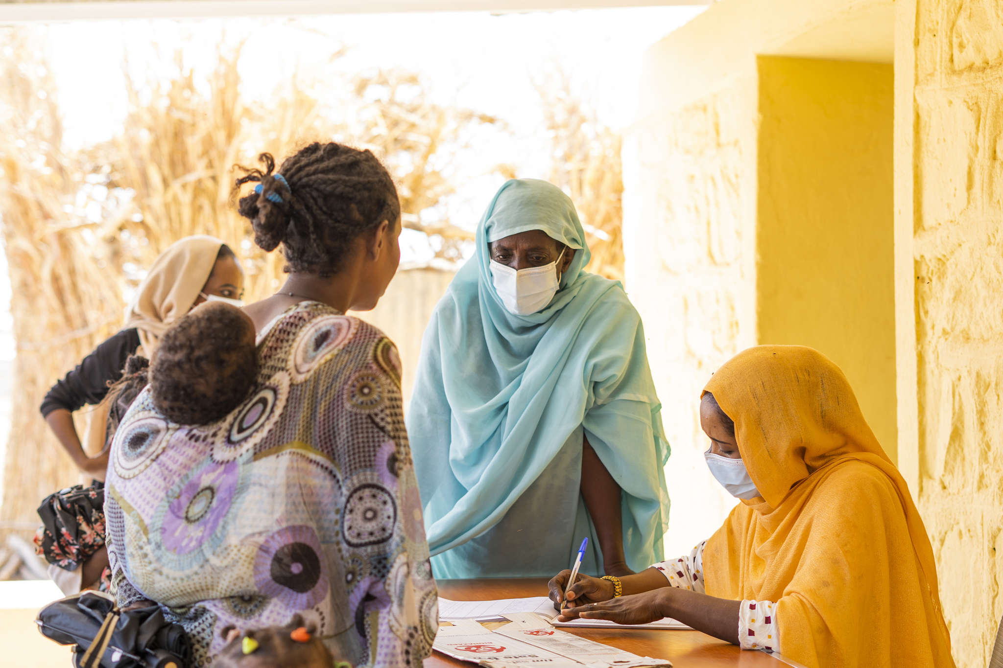 A person carrying a child speaking with two people at a table completing forms. 