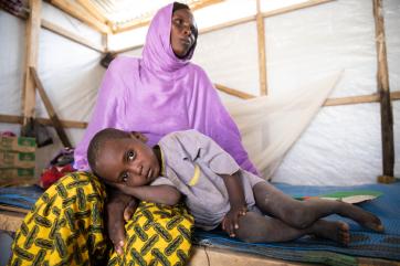 A woman wearing  yellow and purple sits with her son lying on her lap in nigeria