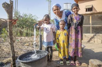 A mother and her daughters collecting water from an outdoor tap.